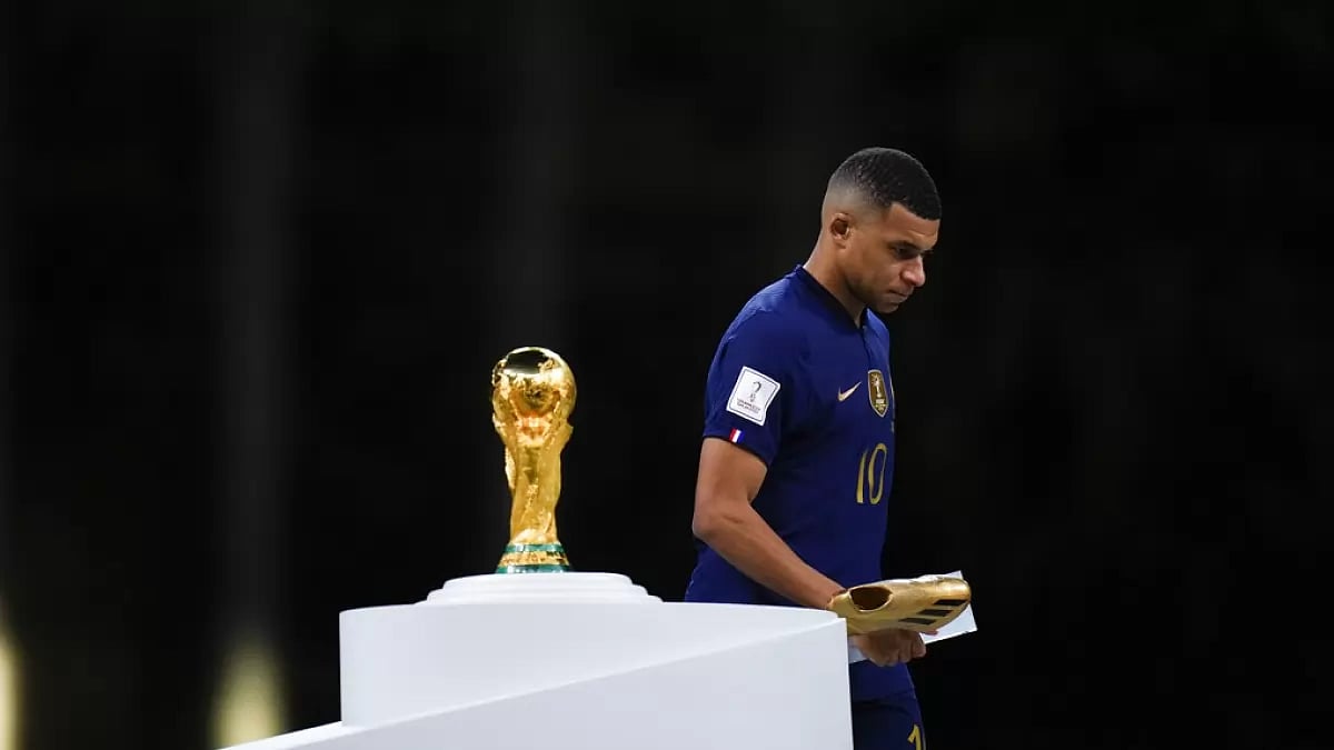 France's Mbappe holds the Golden Boot award as he walks past the World Cup trophy.