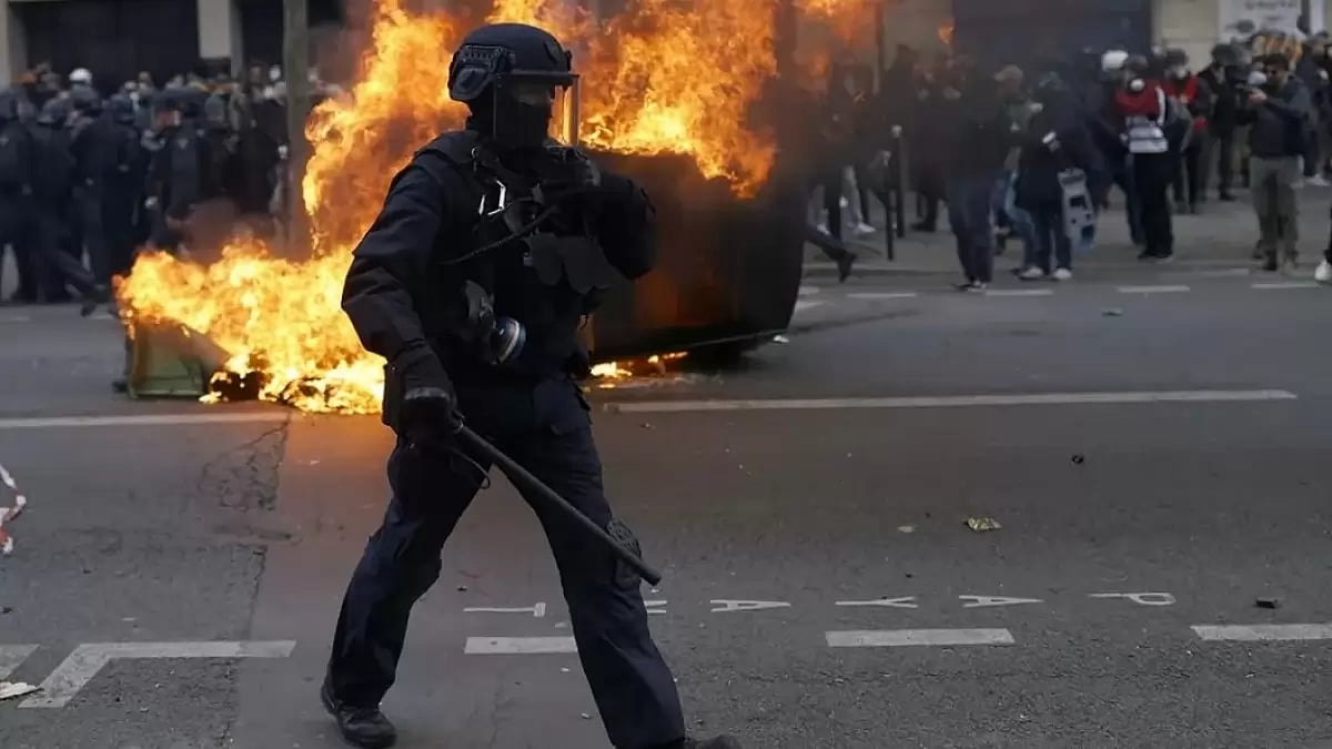 A police officer walks by a burning car during clashes at a demonstration in Paris