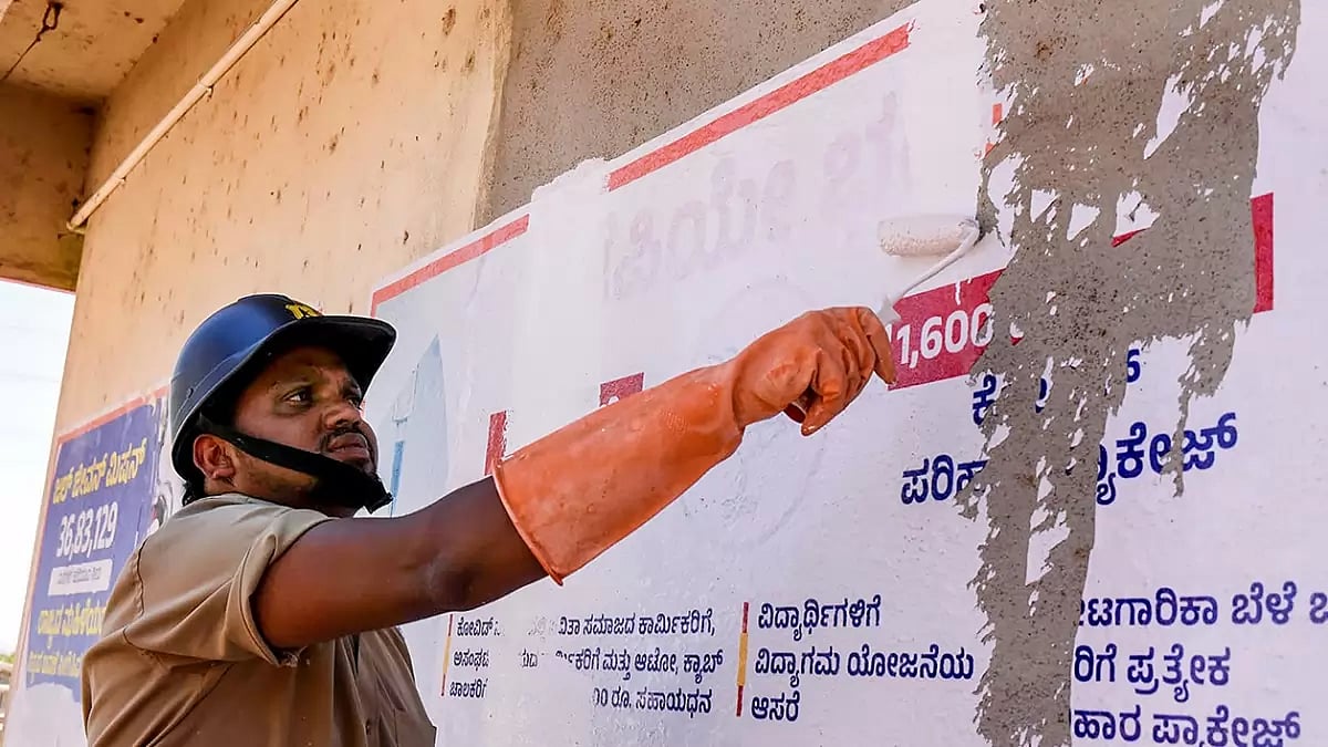 A municipal worker paints political posters on a wall as the Model Code of Conduct has come into effect