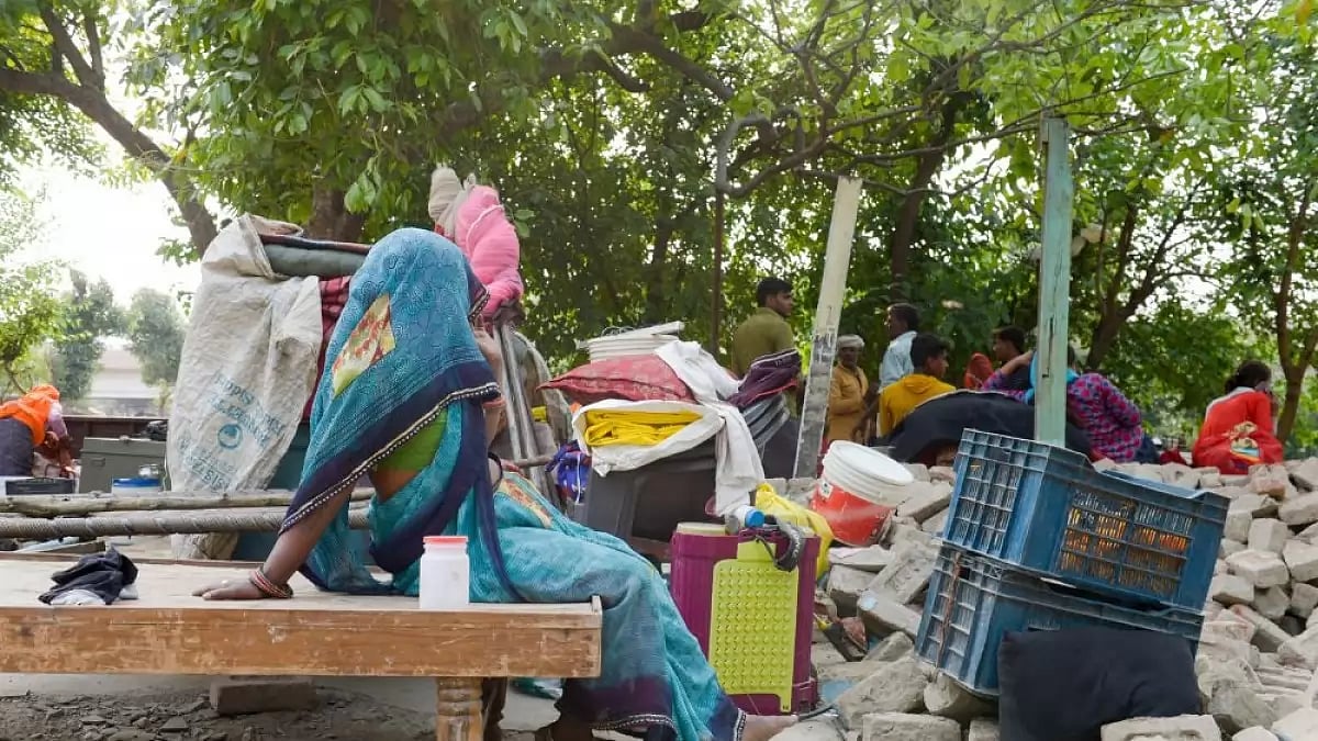 A woman sits on the bed amid the ruins of her demolished house in Moolchand Colony