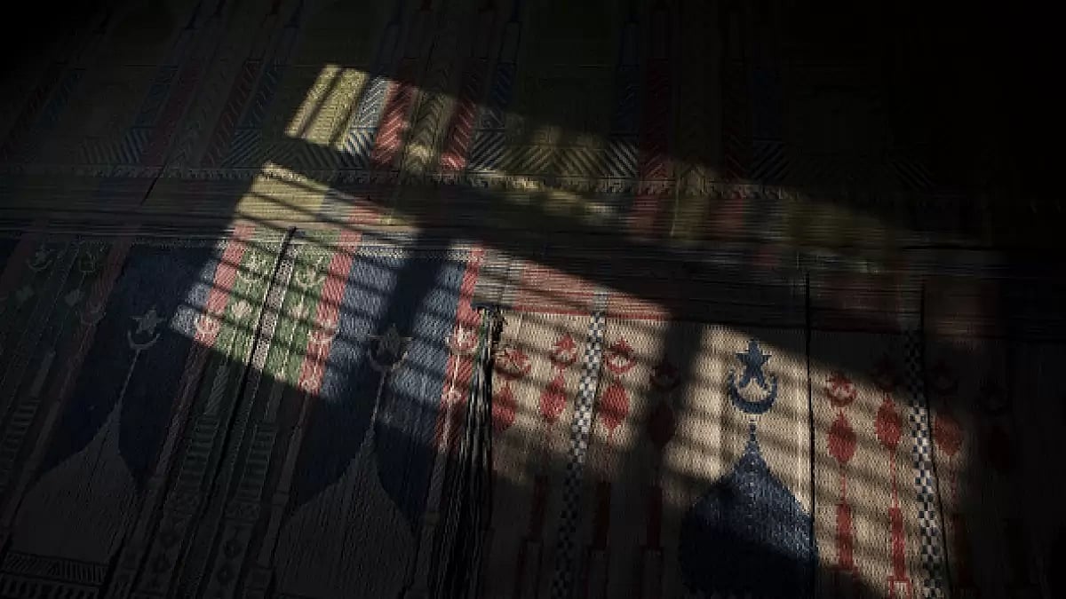 The shadow of a window frame is cast on the carpeted floor of a mosque.