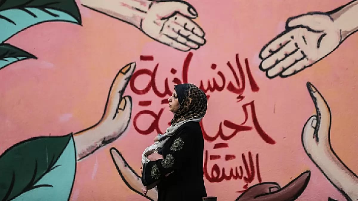 A Palestinian woman carrying her child walks in front of a mural