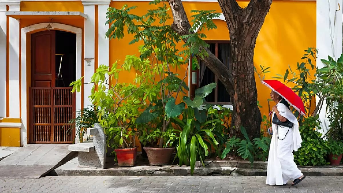 Indian woman in white sari walking by a colorful house in Pondicherry