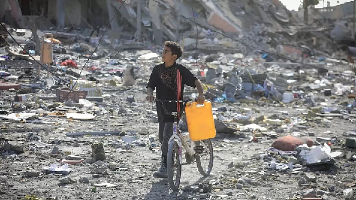 A Palestinian child holds a jerry can as he steers his bicycle around destroyed buildings in Al-Zahra City