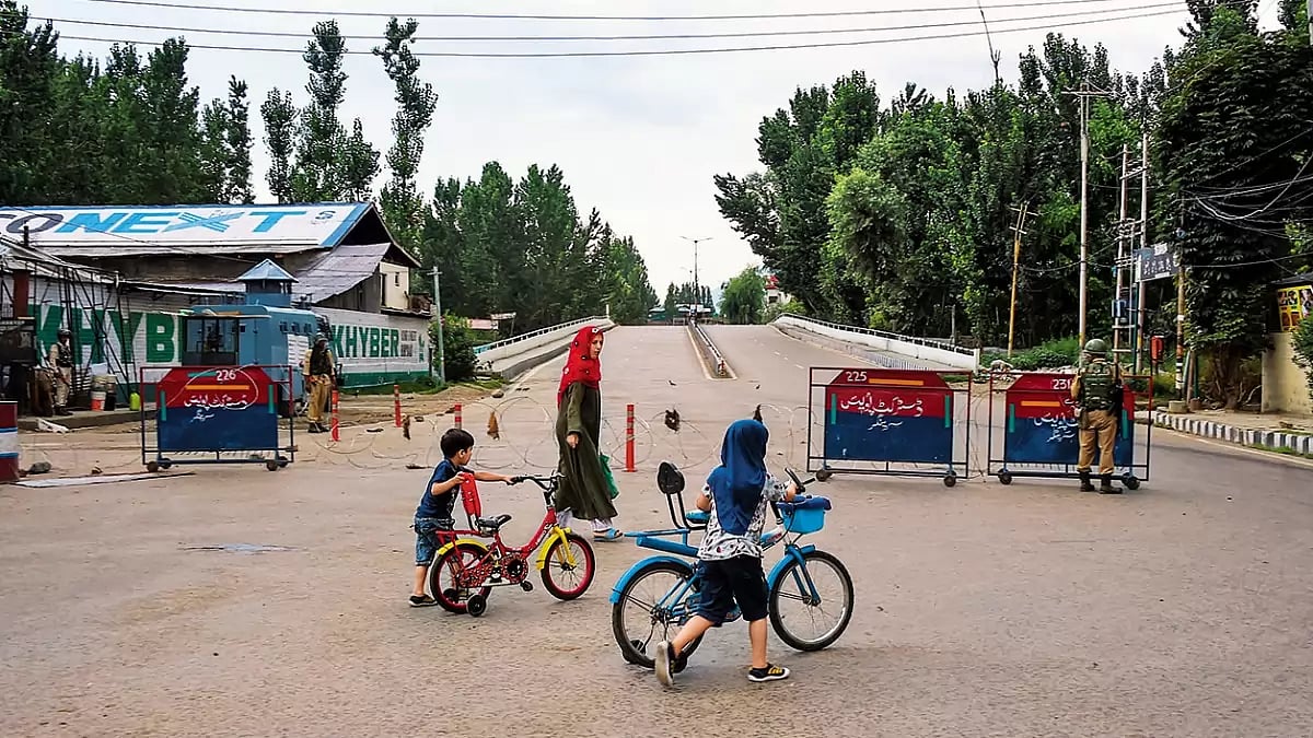 The Kashmir Life: A woman walks with her children as security personnel stand guard 