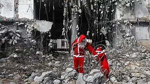 A Palestinian dressed as Santa Claus with his child walk past the al-Jawhara Tower in Gaza City.