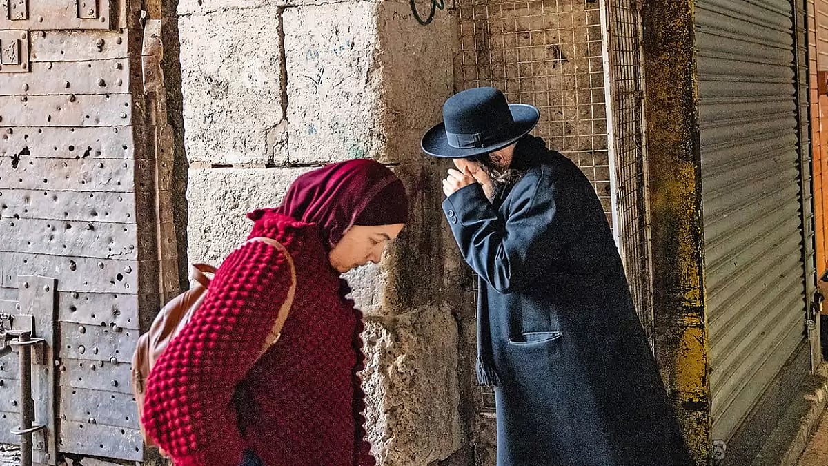 Two Neighbours: A Palestinian woman and an orthodox Jewish man walk past each other in the Old City, Jerusalem