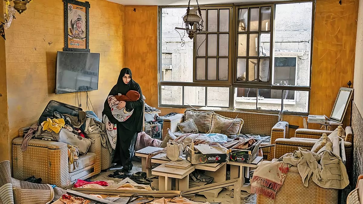 Bank of Targets: A Palestinian woman holds her child after an Israeli strike on her neighbourhood in Gaza Strip