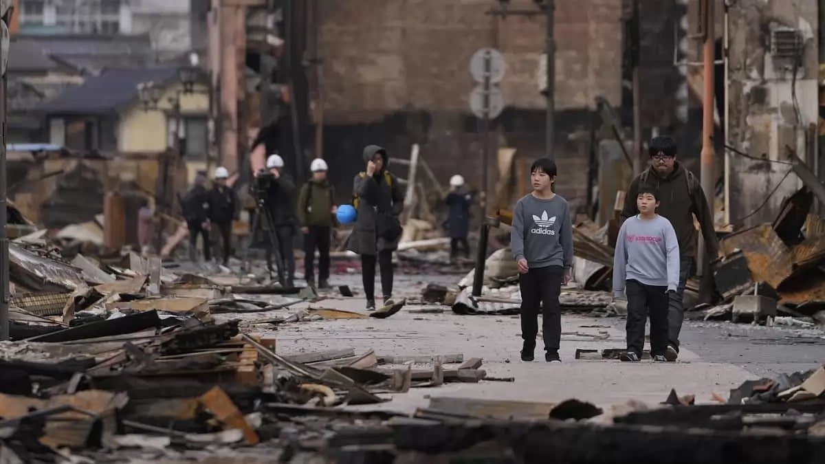 People walk through debris after a fire at shopping area in Wajima in Noto Peninsula after Monday's 