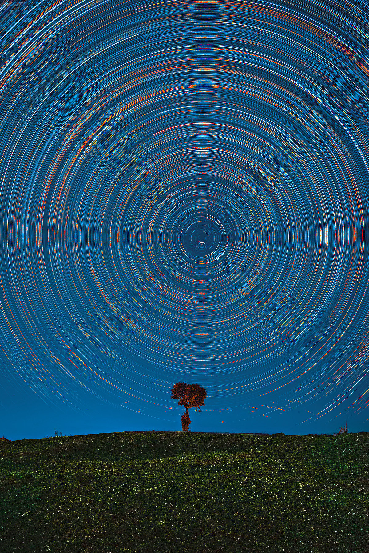 A three-hour-long star trail shot showing the earths motion around its axis. The streaks at the bottom are the flaring up of satellites that crossed the frame