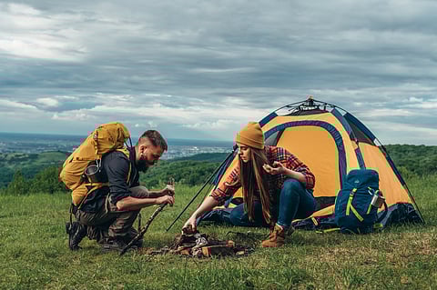 Campers lighting a fire while setting up the camp tent