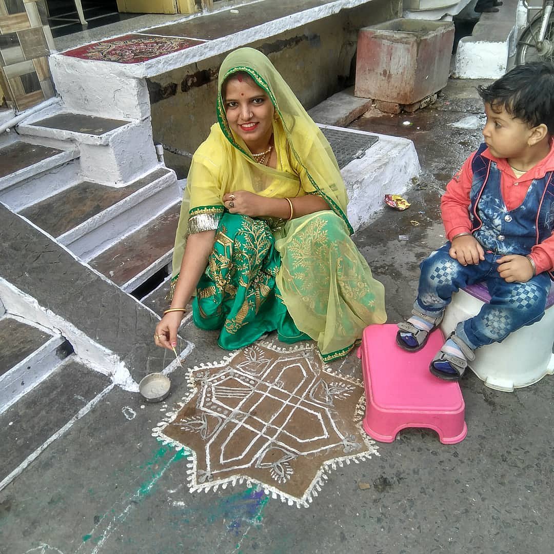 A woman making Mandana rangoli outside her house