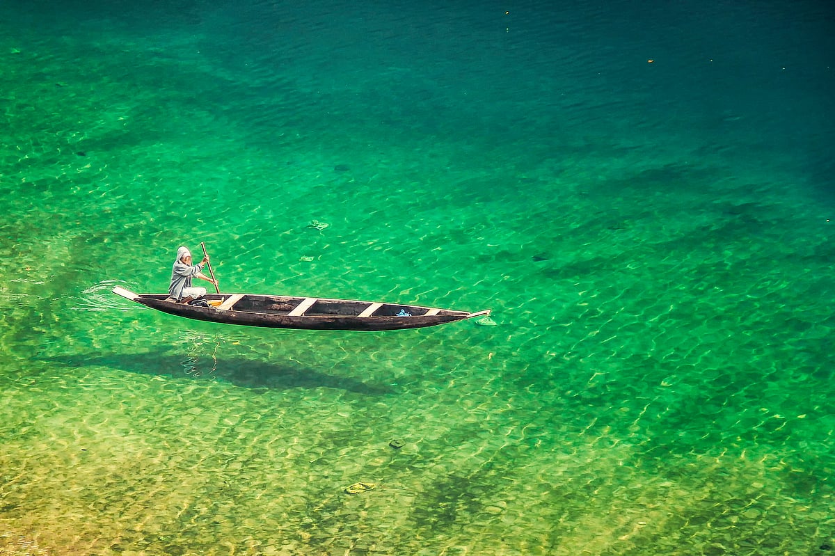 A man rowing across the emerald green Dawki Lake 