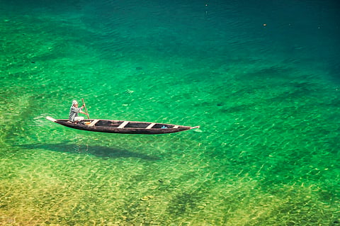 A man rowing across the emerald green Dawki Lake 