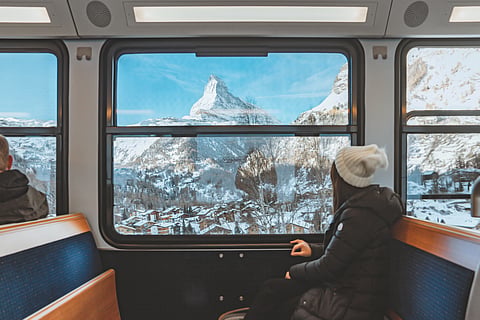young woman traveling looking out the window enjoying in Swiss Alps with the Matterhorn in winter background