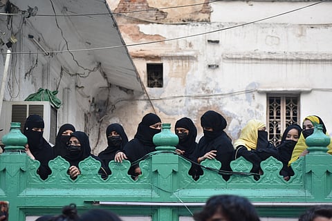 Women from the neighbourhood observe the proceeding from the courtyard