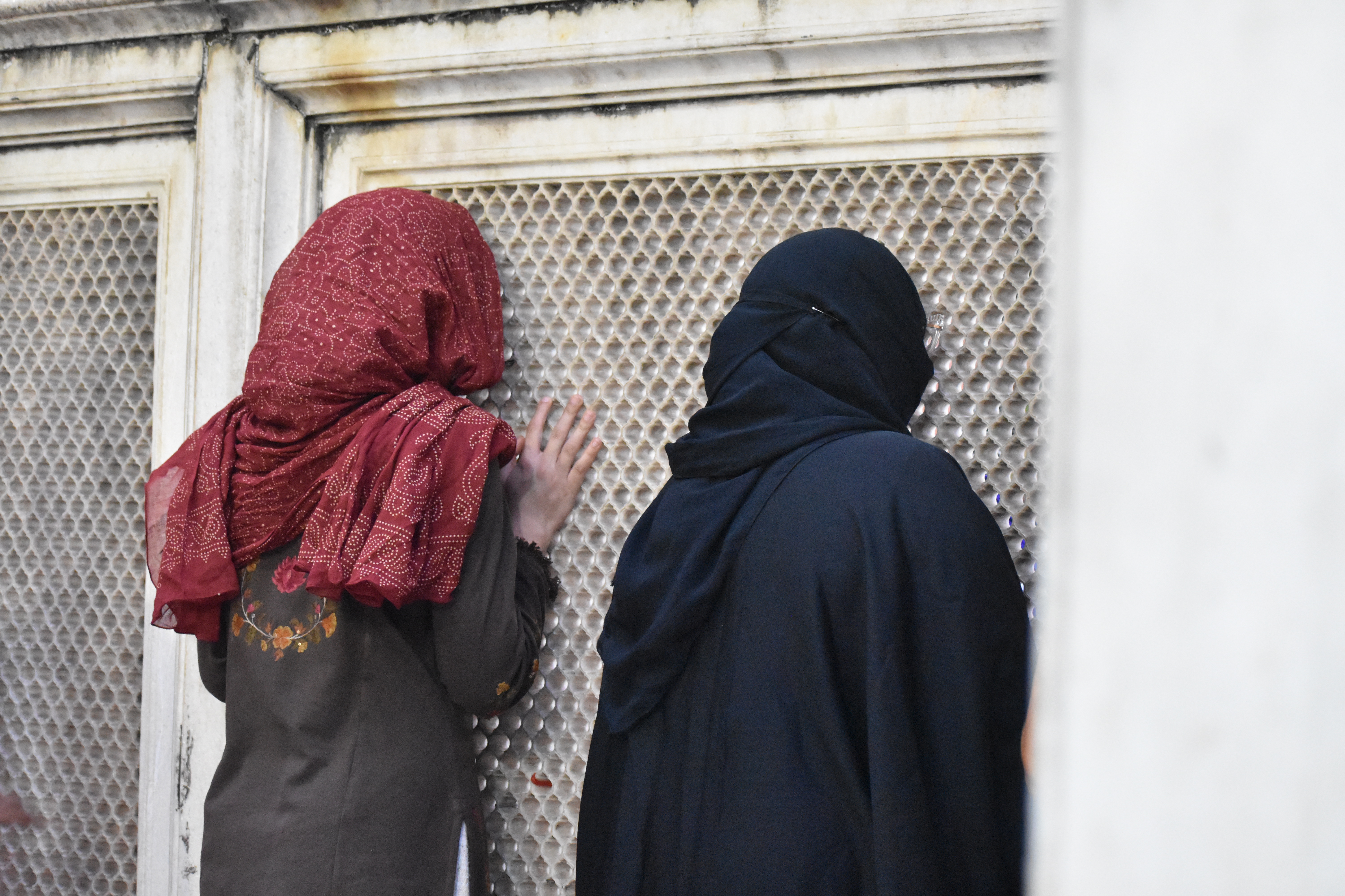 Women stand at the dargha whispering their prayers through the jaali