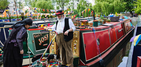 A senior couple in vintage costume and their dog participate in the Canalway Cavalcade of traditional boats in Little Venice