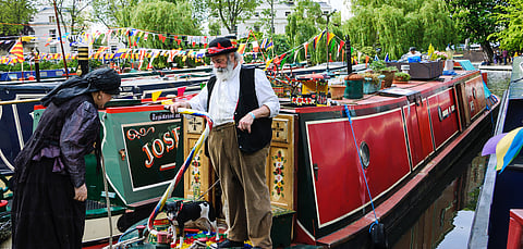 A senior couple in vintage costume and their dog participate in the Canalway Cavalcade of traditional boats in Little Venice