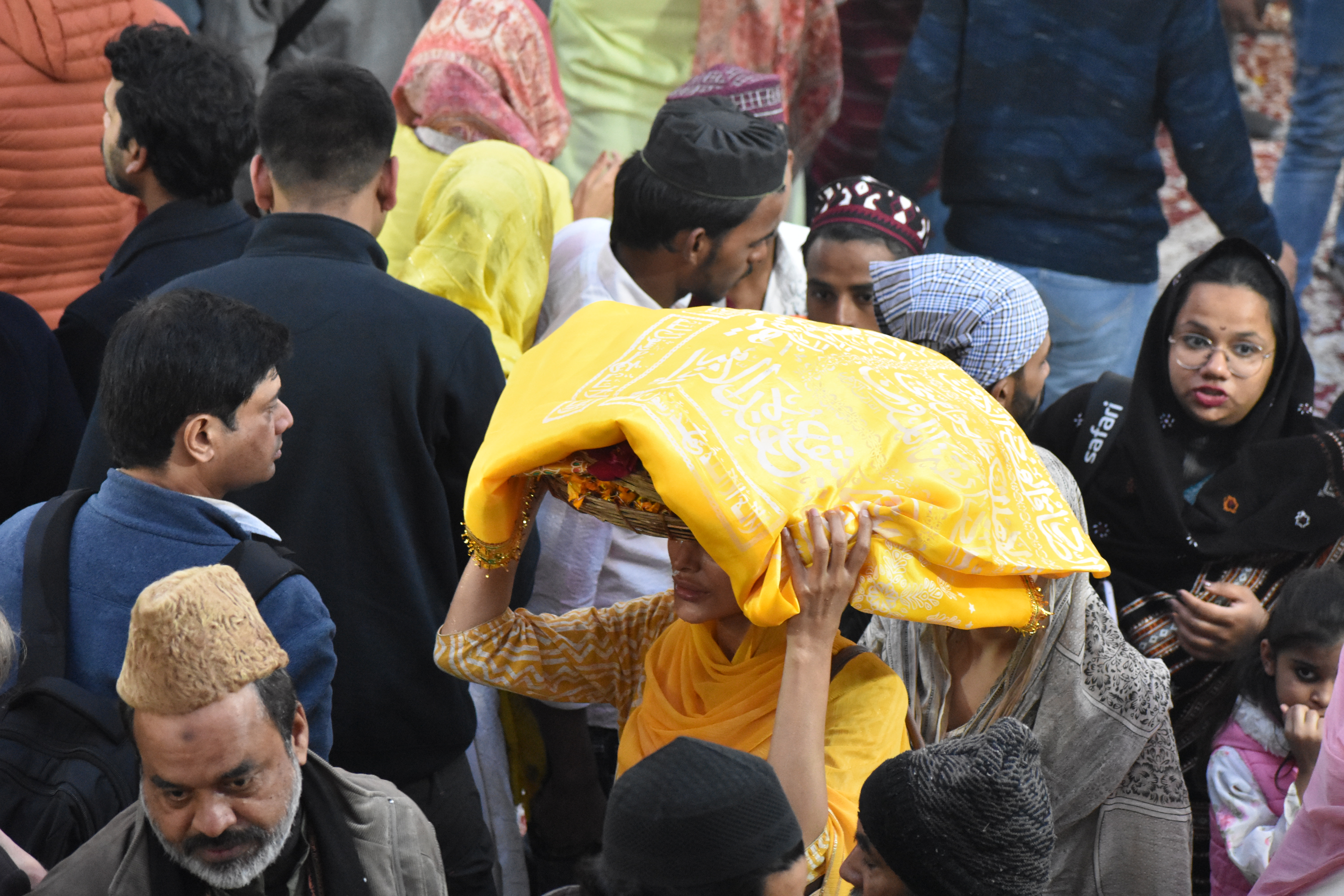 A woman carries a basket of flowers and a yellow scriptured sheet on her head to make offerings