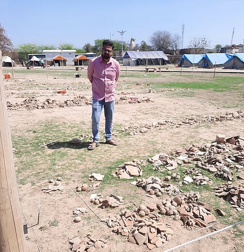 Prakash stands among the grids of objects such as pottery