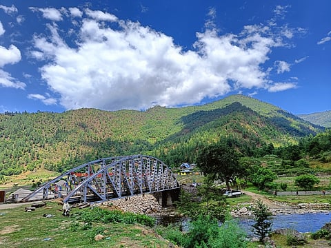 The Landon Bridge in Sangti Valley adorned with colourful prayer flags, stretches across a tranquil river