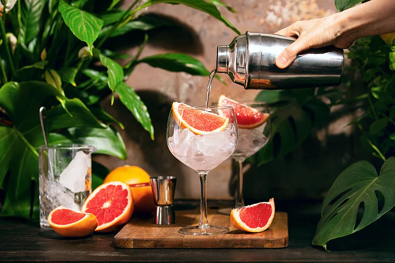 A mixologist prepares a pink grapefruit and rosemary gin cocktail - Shutterstock