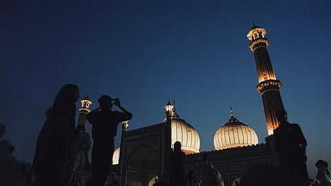 The mosque glows against the night sky, a beacon of faith. Inside, worshippers are in quiet prayer, while outside, children capture the dazzling sight with their cameras.