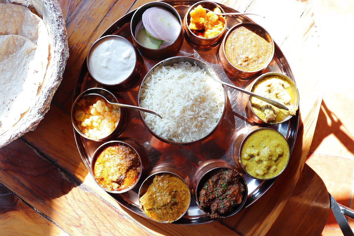 Himachali kangri dham thali includes Kaddu ka khatta, Chane ka Madra, sepu vadi, maash dal, Rajma, salad, rice, or Mitha Bhaat served with Roti and pickle