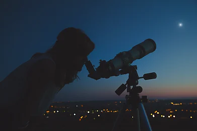 AstroStar/Shutterstock.com : A woman looks through a telescope at the night sky