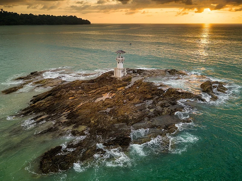 Aerial view of a tropical sunset with a lighthouse in the foreground in Khao Lak