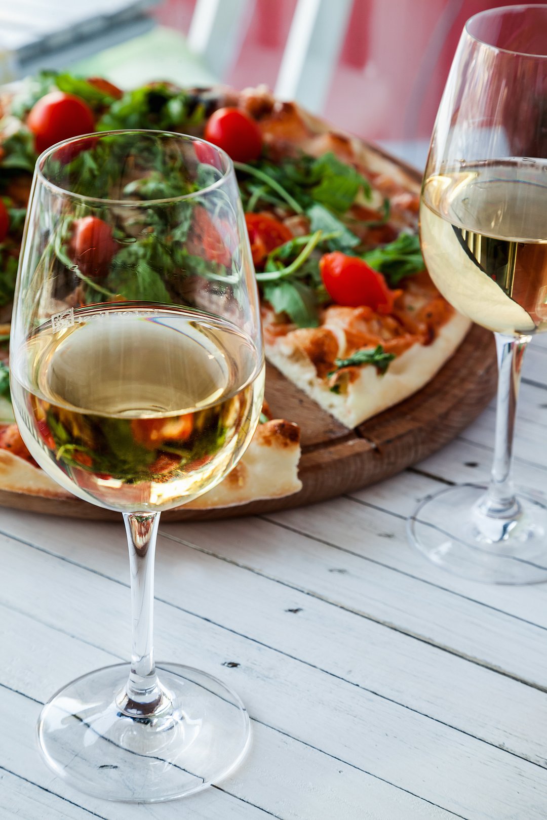 Two glasses of Italian white wine and a pizza on a wooden board