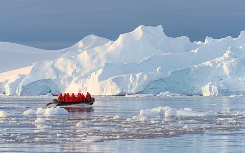 Cruise passengers in red parkas ride in an inflatable boat near an iceberg