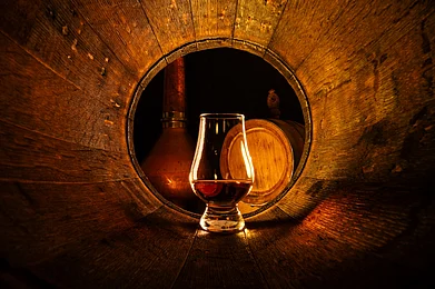 Smit/Shutterstock : A glass of whiskey in an old oak barrel
