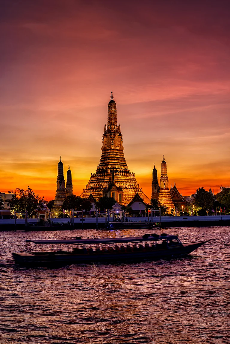 The famous Buddhist Temple Wat Arun during dusk with boat traffic on the Chao Phraya Rriver - Shutterstock
