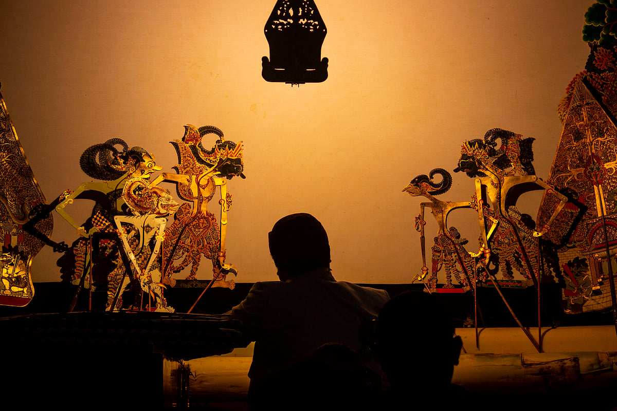 The dalang (master puppeteer) manipulates the carved leather figures between the lamp and screen to bring the shadows to life