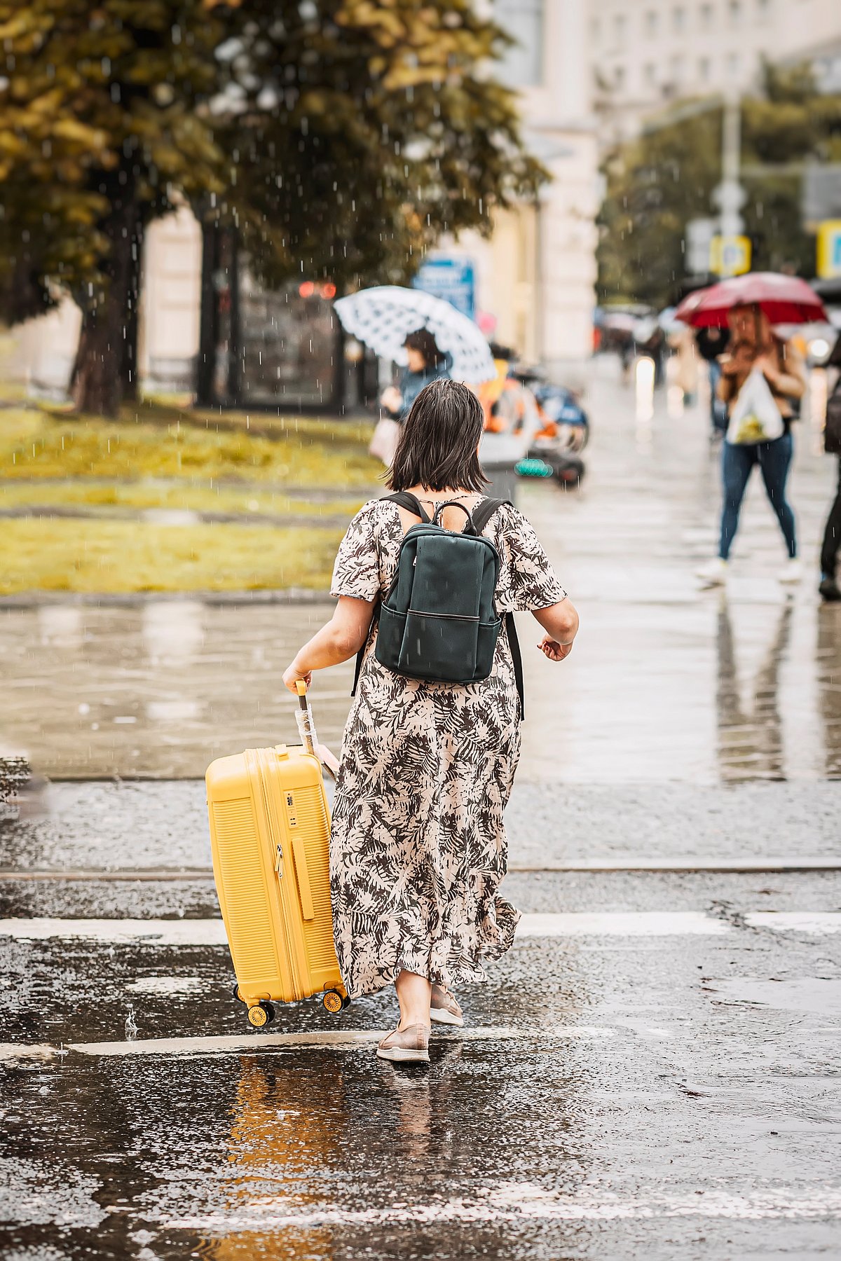 Shutterstock : A woman travelling with a yellow trolley suitcase in the rain