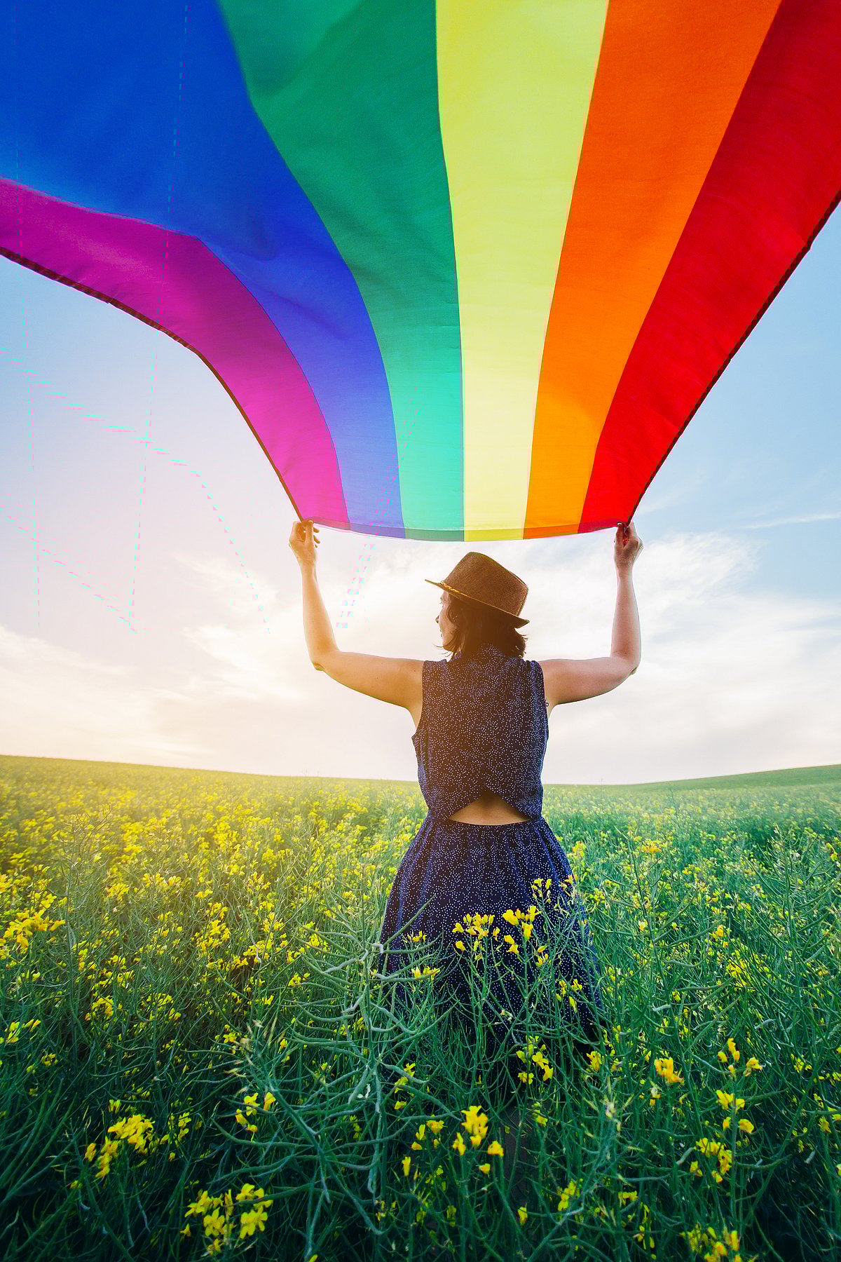 Shutterstock : Woman holding the Gay Rainbow Flag on a green meadow outdoors