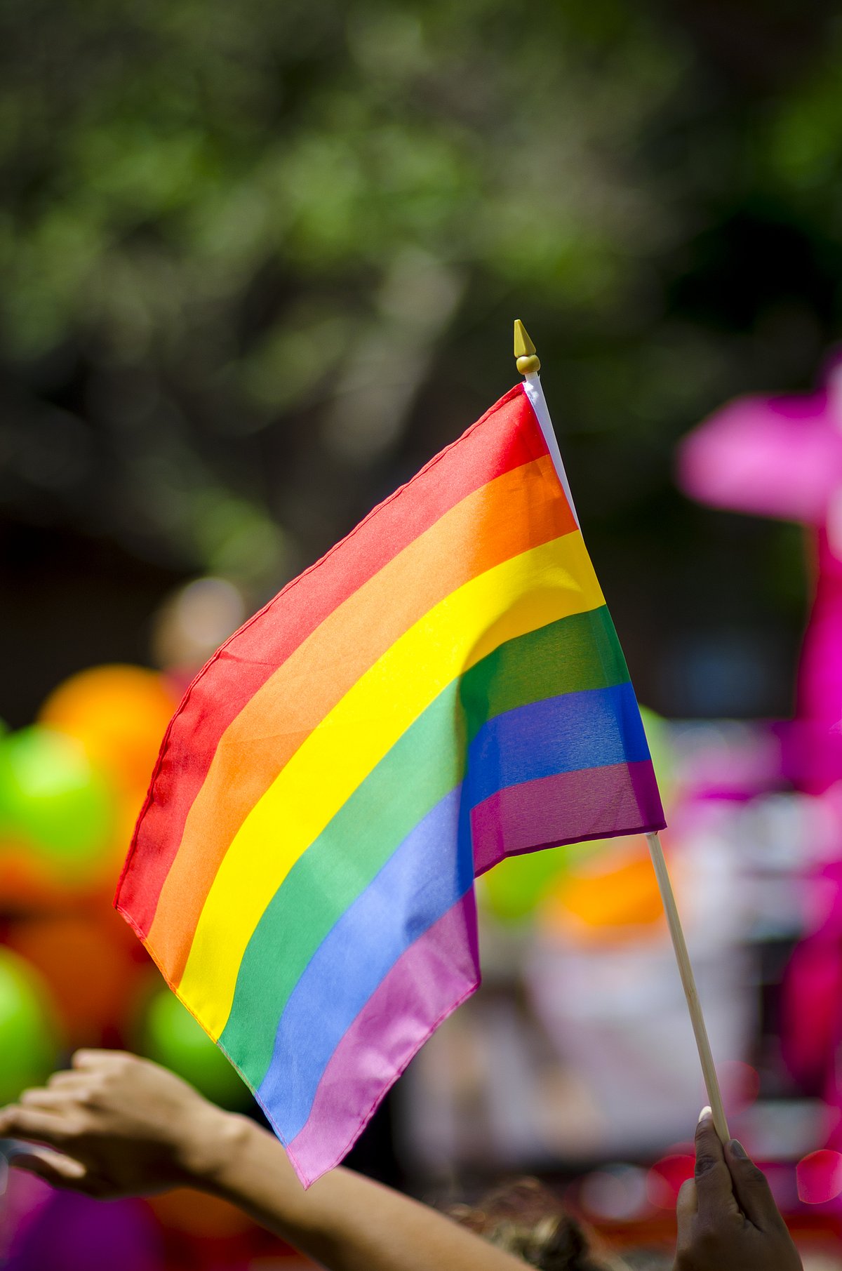 Shutterstock : A rainbow flag flying in bright sun on the sidelines of a colorful summer gay pride parade