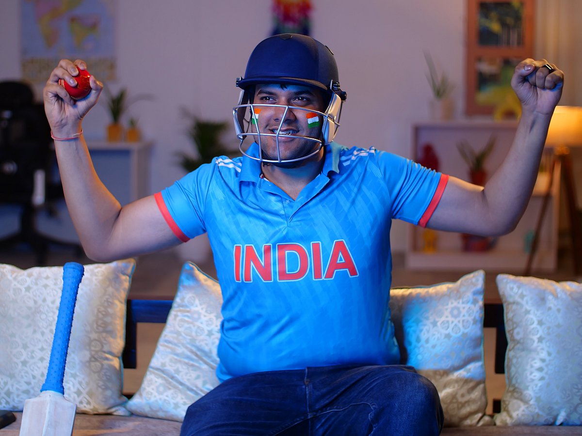 Excited young Indian man wearing cricket jersey and helmet