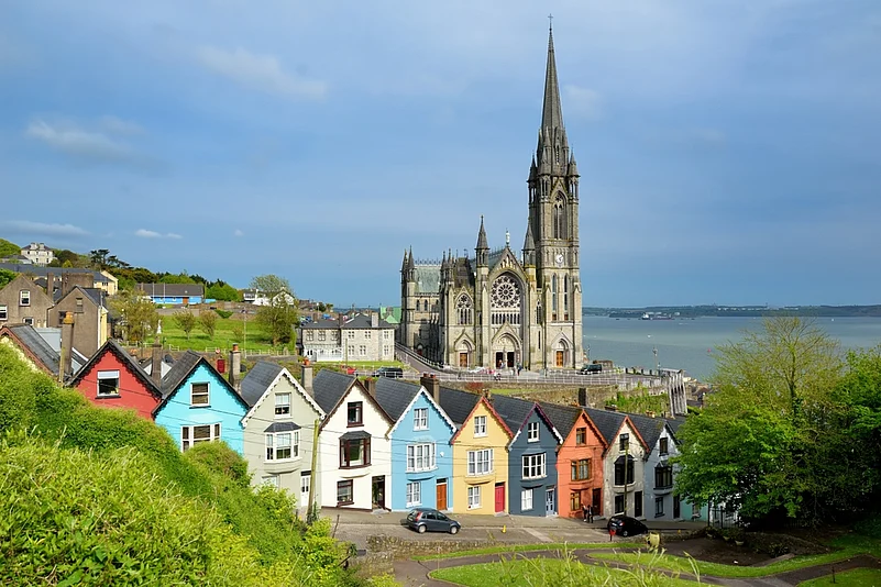 Colourful row houses with towering St. Colmans Cathedral in background in the port town of Cobh, County Cork, Ireland