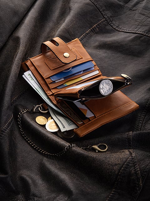 Compact brown leather wallet filled with cards and bills, featuring zippered coin pocket and secure anti-theft chain