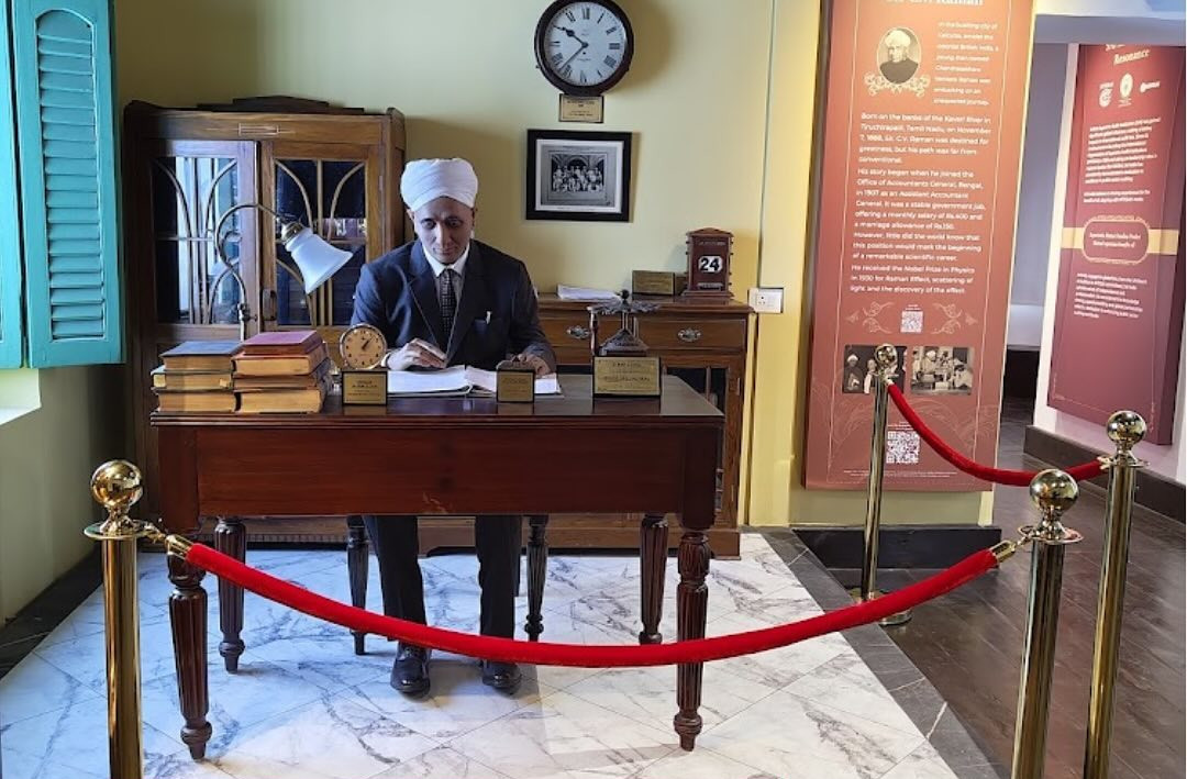 A statue of Sir C V Raman sitting on the desk and chair he used in 1907