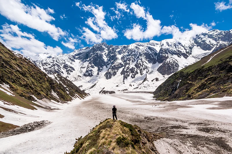 A lone hiker looks at the view of the Himalayas on the Beas Kund trek