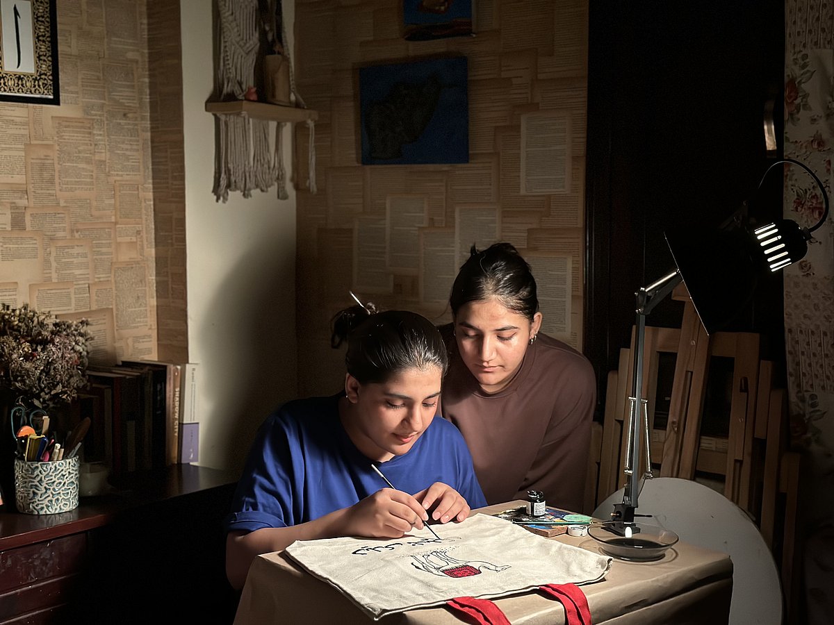 Copyright: Anar Studio : Maryam Kakar (left) paints a tote bag with Heela Kakar next to her