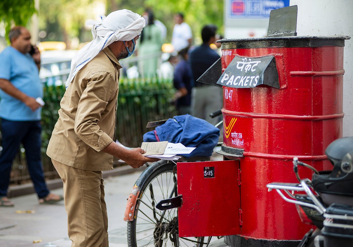 An Indian postal worker collecting mail from a letter box in 2022