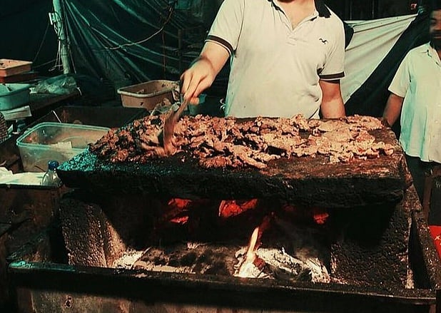 The making of Patthar ka Gosht involves slowly cooking meat on a large stone slab heated using firewood