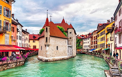 People walk near the Thiou canal in Old Town of Annecy in France, encircling the medieval palace, Palais de l'Isle