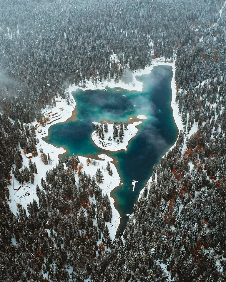A lake surrounded by snow-covered trees in Caumasee, Switzerland - Shutterstock
