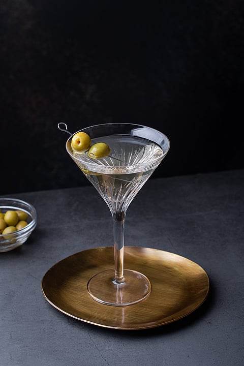 Dirty martini cocktail in martini glass with olives garnish on dark table